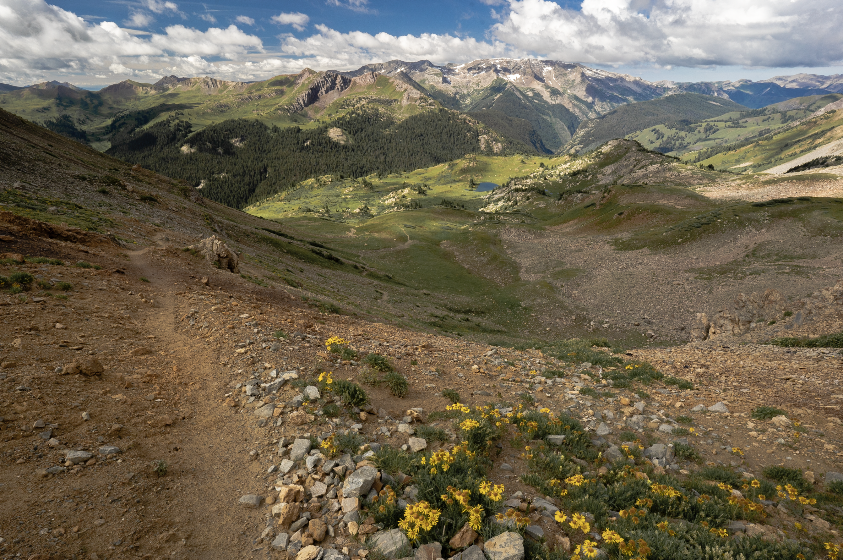 Panoramic view atop Trail Rider pass looking at the trail down below as it passes a scenic alpine lake