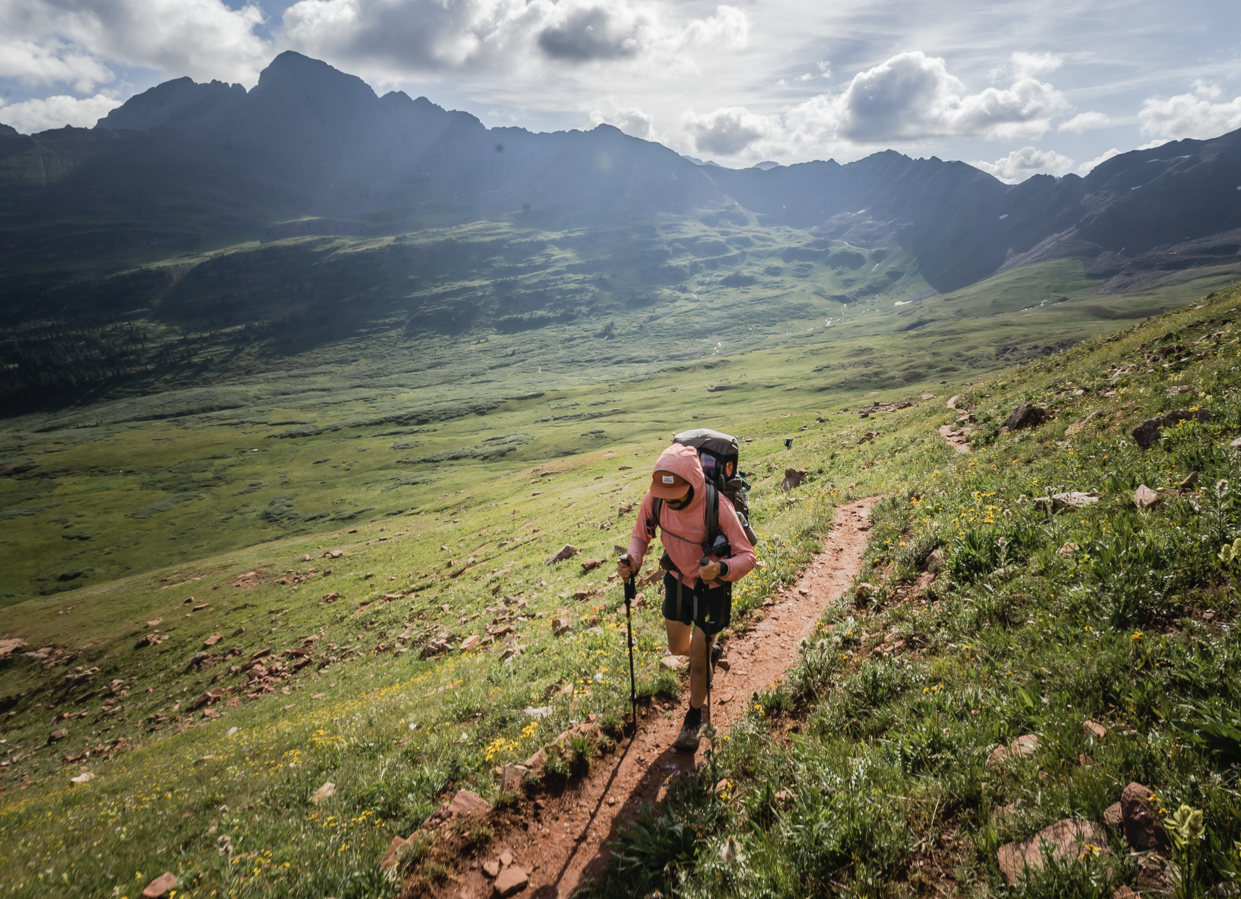 A hiker passes the photographer on trail with a sunny mountain landscape in the background